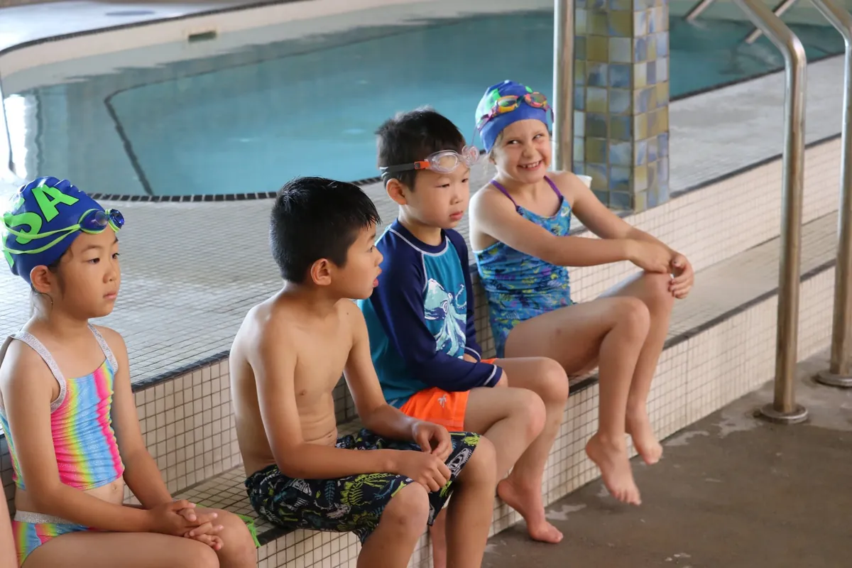 Blue-level swimmers sitting beside the pool